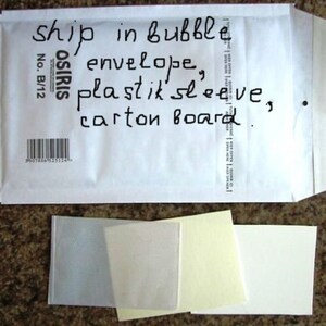 May include: A white bubble envelope with handwritten text and a barcode. Below the envelope are several small, clear and white rectangular pieces of paper.