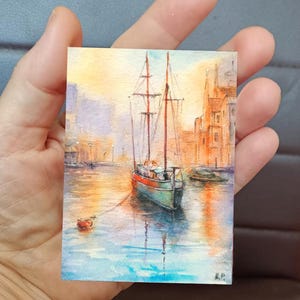 This ACEO painting (6 × 9 cm) captures a peaceful boat ride through a glowing marine, surrounded by warm architecture and reflections on water. The soft light and expressive brushwork create a romantic art.