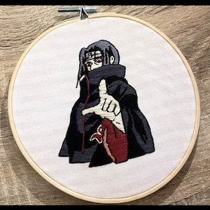May include: Embroidered hoop art featuring a black-clad anime character with red eyes and a red scarf. The character is making a hand gesture with their right hand.