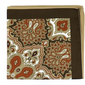 May include: A folded pocket square with a paisley pattern in shades of brown, tan, and rust. The central design features intricate paisley shapes against a white background. A dark brown border frames the pattern, with a tan edge.