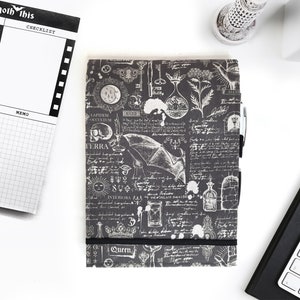 May include: A black and white planner with a gothic design. The cover features a bat, a skull, and other occult symbols. The planner has a checklist and memo section. The text "you goth this" is printed on the cover.