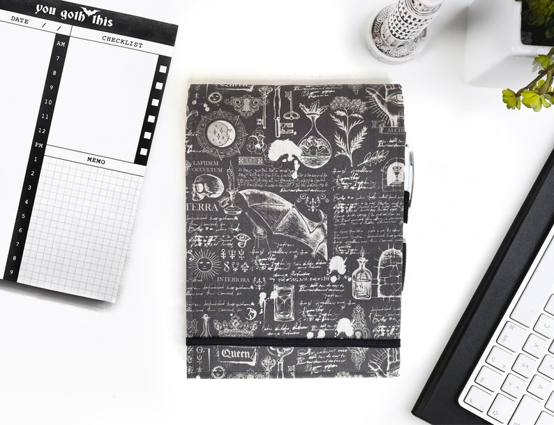 May include: A black and white planner with a gothic design. The cover features a bat, a skull, and other occult symbols. The planner has a checklist and memo section. The text "you goth this" is printed on the cover.