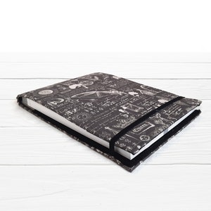 May include: A black and white notebook with a vintage scientific illustration design. The notebook has a black elastic closure and a white paper insert.