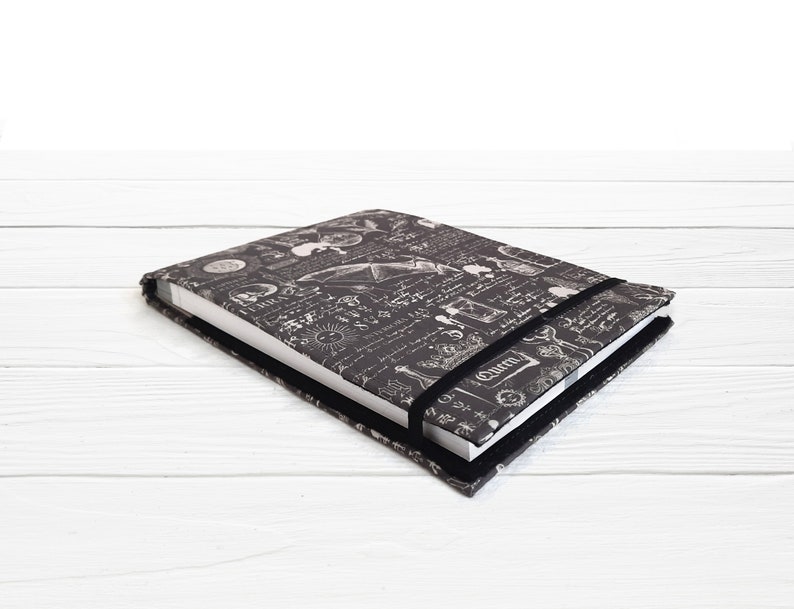 May include: A black and white notebook with a vintage scientific illustration design. The notebook has a black elastic closure and a white paper insert.