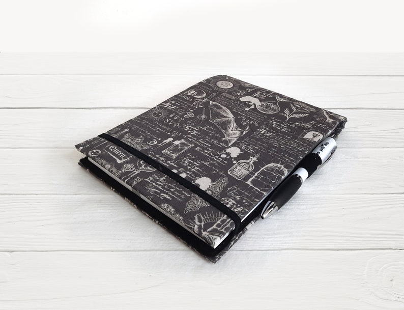 May include: A black and white journal with a gothic design featuring a bat, a skull, and other occult symbols. The journal has a black elastic closure and a black pen is included.