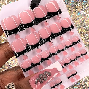 May include: A set of 20 pink and black press-on nails with a white accent nail featuring the word "2000" in silver glitter. The nails are arranged on a white card.