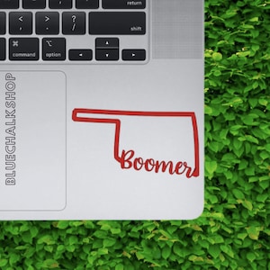 May include: Red vinyl sticker of the state of Oklahoma with the word "Boomer" written in a cursive font.