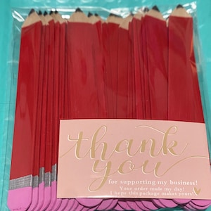 K&ouml;nnte beinhalten: Eine Dankeskarte mit rosa Hintergrund und goldenen Schriftz&uuml;gen, auf der "Danke" und "f&uuml;r die Unterst&uuml;tzung meines Gesch&auml;fts! Ihre Bestellung hat meinen Tag gerettet! Ich hoffe, dieses Paket macht Ihren Tag!" steht. Die Karte ist von einem Stapel roter und rosa Stifte aus Bastelholz umgeben.