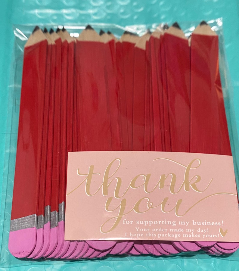K&ouml;nnte beinhalten: Eine Dankeskarte mit rosa Hintergrund und goldenen Schriftz&uuml;gen, auf der "Danke" und "f&uuml;r die Unterst&uuml;tzung meines Gesch&auml;fts! Ihre Bestellung hat meinen Tag gerettet! Ich hoffe, dieses Paket macht Ihren Tag!" steht. Die Karte ist von einem Stapel roter und rosa Stifte aus Bastelholz umgeben.