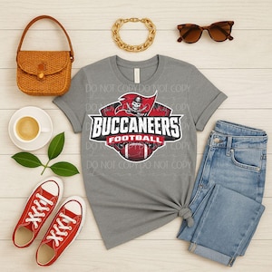 Puede incluir: Una camiseta gris con el texto "BUCCANEERS FOOTBALL" y un logotipo del equipo con una calavera pirata y un balón de fútbol. La imagen también incluye zapatillas rojas, vaqueros azules, un bolso tejido, gafas de sol y una pulsera de cadena dorada.