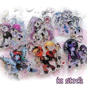 Könnte beinhalten: Eine Sammlung klarer Acryl-Schlüsselanhänger mit stilisierten Pony-Illustrationen in verschiedenen Farbschemata. Jeder Schlüsselanhänger hat einen Metallverschluss. Der Text "in stock" ist unten rechts sichtbar.