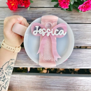 May include: A pink and white ceramic mug with a pink glitter bow and the name "Jessica" written on it.