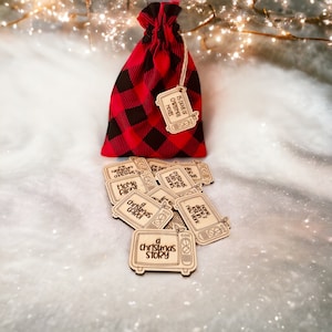 Könnte beinhalten: Eine rote und schwarze karierte Tasche mit einem Etikett, auf dem "25 Tage Weihnachtsfilme" steht. Die Tasche ist gefüllt mit Holzschmuck in Form von alten Fernsehern, jeder mit einem anderen Weihnachtsfilmtitel. Die Titel beinhalten "Kevin - Allein zu Haus", "Eine Weihnachtsgeschichte", "Es war einmal in Amerika", "Der Weihnachtswalzer", "Ist das Leben nicht schön?" und "Eine Weihnachtsgeschichte".