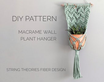 May include: A sage green macrame wall plant hanger featuring a chevron knot pattern suspended from a wooden branch, holding a terracotta pot with a green plant. Text reads: DIY PATTERN MACRAME WALL PLANT HANGER STRING THEORIES FIBER DESIGN.