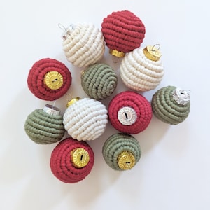 Op de afbeelding: Een verzameling handgemaakte kerstversieringen in rood, wit en groen. De ornamenten zijn gemaakt van garen en hebben een gouden top.