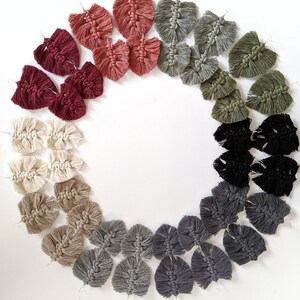 May include: A set of 20 handmade macrame earrings in various colours, including red, green, black, grey, and beige. The earrings are shaped like leaves and are arranged in a circle.
