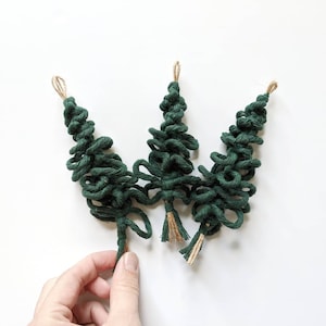 May include: Three green yarn Christmas tree ornaments with brown twine accents.