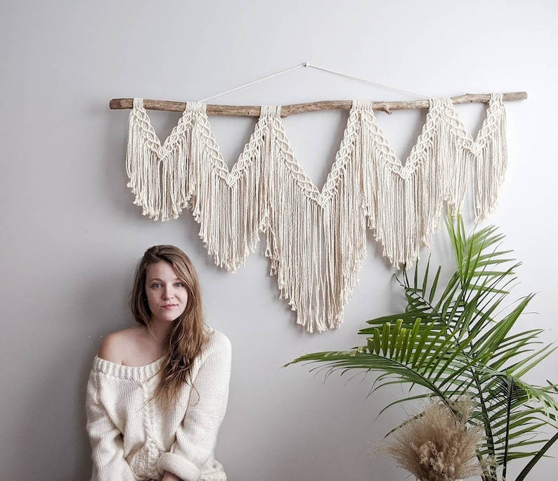 Pode incluir: Uma tape&ccedil;aria de macram&eacute; branca com um ramo de madeira e um design tecido. A tape&ccedil;aria &eacute; feita de cord&atilde;o de algod&atilde;o e tem um estilo bo&ecirc;mio.