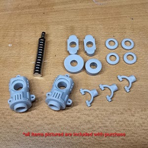 May include: A collection of gray plastic model parts including two main housing components, a cylindrical metal rod, two flat circular discs, two rectangular pieces with holes, four small rings, and three Y-shaped connectors with the text all items pictured are included with purchase.