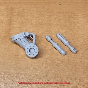 Könnte beinhalten: Ein Set aus drei unbemalten grauen Miniaturbauteilen aus Kunstharz, bestehend aus einem mechanischen Armteil mit kreisförmigem Gelenk und einem flexiblen Schlauch sowie zwei separaten zylindrischen Waffenaufsätzen mit gerippten Details.