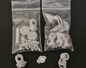 May include: Two clear plastic resealable bags containing various small gray resin model parts, including cylindrical components, circular joints, and a tube of small silver magnets, with additional loose parts placed outside the bags.