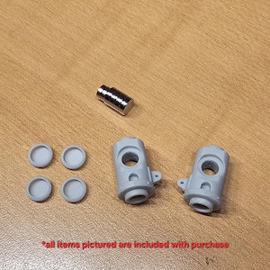 May include: A set of components including one small metallic cylindrical magnet, two identical light gray plastic mechanical housings with circular openings, and four small light gray circular plastic caps. The text reads: all items pictured are included with purchase.