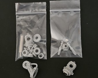 May include: Two clear plastic bags containing small gray resin model parts, including circular discs, cylindrical components, and mechanical structures. Two additional loose gray mechanical parts are positioned outside the bags.
