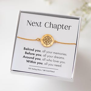 Könnte beinhalten: Ein goldfarbenes Kompassarmband auf einer weißen Karte mit der Aufschrift "Next Chapter". Die Karte enthält auch den Text "Hinter dir, all deine Erinnerungen. Vor dir, all deine Träume. Um dich herum, alle, die dich lieben. In dir, alles, was du brauchst."