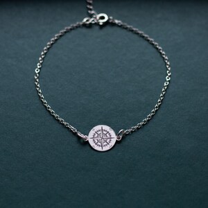 Puede incluir: Una pulsera de cadena plateada con un dije circular en el centro. El dije est&aacute; grabado con un dise&ntilde;o detallado de rosa de los vientos, incluyendo los puntos cardinales N, S, E y O. La pulsera incluye un peque&ntilde;o cierre de mosquet&oacute;n.
