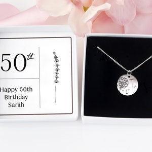 May include: A silver necklace with a round pendant featuring a dandelion design, presented in a white gift box with a black interior. The box lid displays the text "50th Happy 50th Birthday Sarah".