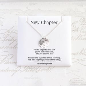 May include: A silver necklace with a round pendant featuring a dandelion design. The pendant hangs from a delicate chain and is displayed on a white card with the text "New Chapter" and inspirational quotes. The card reads "925 Sterling Silver."