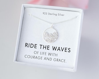 May include: A sterling silver necklace with a circular pendant featuring a wave design. The necklace is displayed in a white box with the text "RIDE THE WAVES OF LIFE WITH COURAGE AND GRACE." The box also states "925 Sterling Silver."