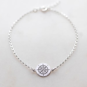 Puede incluir: Una pulsera de cadena plateada con un dije circular en el centro. El dije est&aacute; grabado con un dise&ntilde;o detallado de rosa de los vientos, que incluye los puntos cardinales N, E, S y O, junto con las marcas NE, SE, SO y NO.