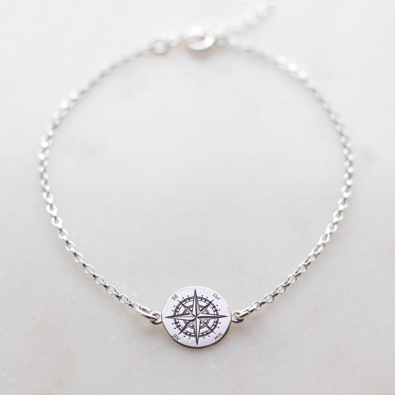 Puede incluir: Una pulsera de cadena plateada con un dije circular en el centro. El dije est&aacute; grabado con un dise&ntilde;o detallado de rosa de los vientos, que incluye los puntos cardinales N, E, S y O, junto con las marcas NE, SE, SO y NO.