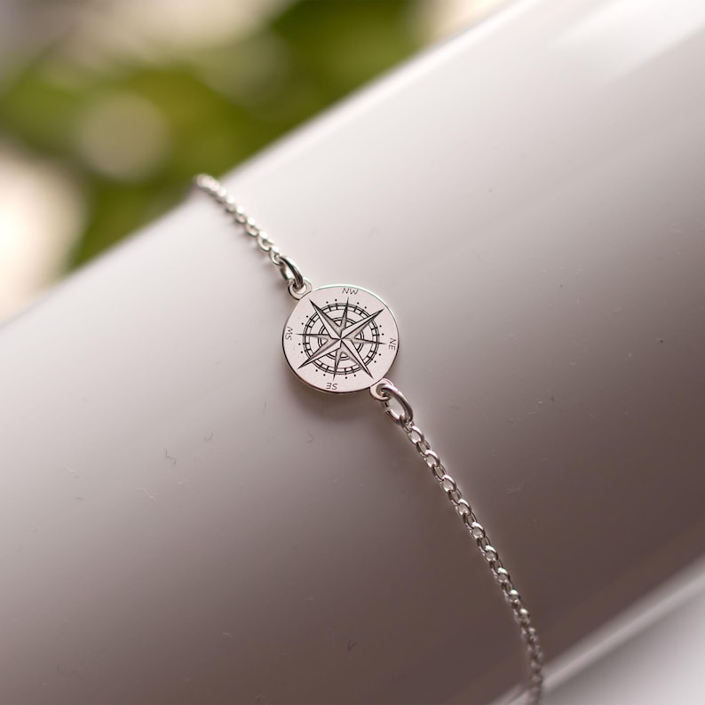 Puede incluir: Una pulsera de cadena en tono plateado con un peque&ntilde;o dije circular grabado con un dise&ntilde;o detallado de rosa de los vientos. El dije de br&uacute;jula muestra los puntos cardinales incluyendo NW, NE, SE y SW, unido a una fina cadena de eslabones.