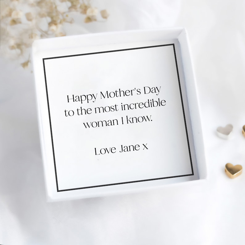 Pode incluir: Uma caixa de presente branca com borda preta cont&eacute;m um cart&atilde;o com o texto "Happy Mother's Day to the most incredible woman I know. Love Jane x". O fundo &eacute; branco com pequenos elementos decorativos.