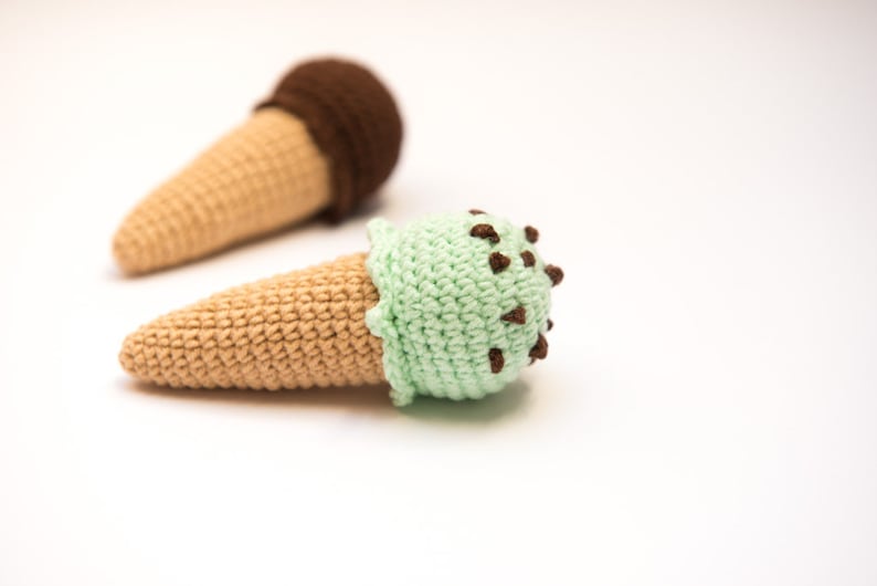 Puede incluir: Dos conos de helado de ganchillo, uno con helado de chocolate y otro con helado de menta con chispas de chocolate.