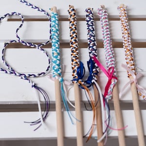 May include: Six colorful braided wands with wooden sticks and ribbon bows. The wands are made with white, blue, orange, pink, and gold thread.