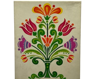 May include: A rectangular white wall art piece featuring a symmetrical floral illustration. The design displays a central orange flower, two pink tulips, and two purple bell-shaped flowers, all connected by green stems and leaves on a white background.