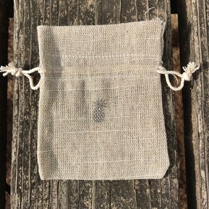 May include: A small, off-white, linen drawstring bag with a simple design. The bag is made of a natural fabric and has a rustic look.