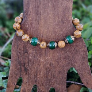 May include: A brown and green beaded bracelet with gold accents. The bracelet is made of round beads with a speckled pattern.