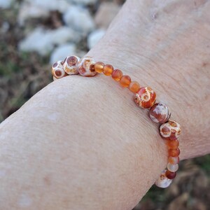 May include: A bracelet featuring brown, white and orange agate beads. The beads are round and have a mottled pattern.