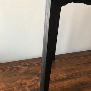 Puede incluir: Taburete de madera negro con un dise&ntilde;o sencillo. El taburete tiene una parte superior cuadrada y cuatro patas.