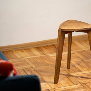 K&ouml;nnte beinhalten: Ein dreibeiniger Hocker aus Holz mit dreieckiger Sitzfl&auml;che, der auf einem Holzboden steht.