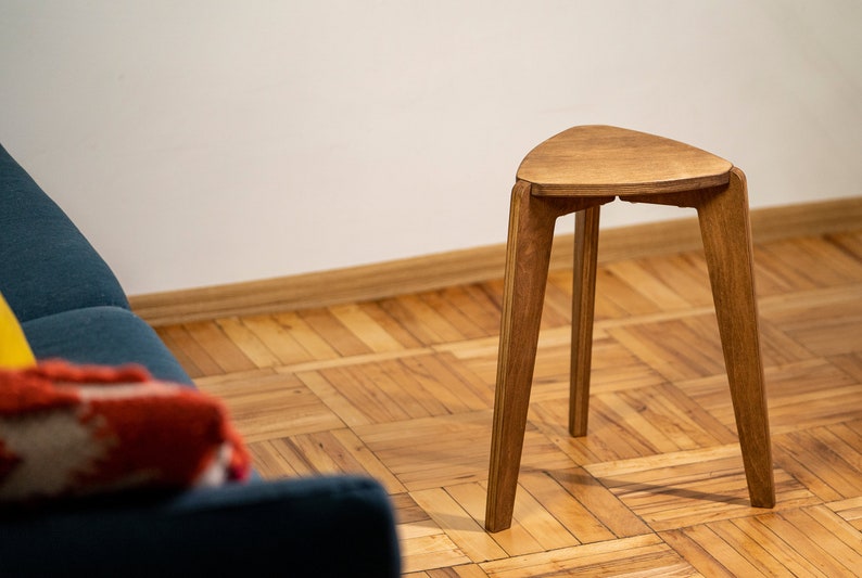 K&ouml;nnte beinhalten: Ein dreibeiniger Hocker aus Holz mit dreieckiger Sitzfl&auml;che, der auf einem Holzboden steht.