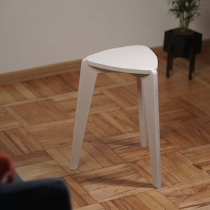 K&ouml;nnte beinhalten: Wei&szlig;er dreieckiger Hocker mit drei Beinen. Der Hocker ist aus Holz und hat ein schlichtes Design.