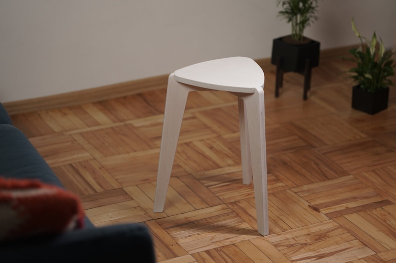 K&ouml;nnte beinhalten: Wei&szlig;er dreieckiger Hocker mit drei Beinen. Der Hocker ist aus Holz und hat ein schlichtes Design.