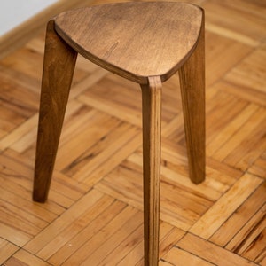 K&ouml;nnte beinhalten: Ein dreibeiniger Hocker aus dreieckigem Holz. Der Hocker ist aus hellem braunem Holz gefertigt und hat eine glatte, polierte Oberfl&auml;che.
