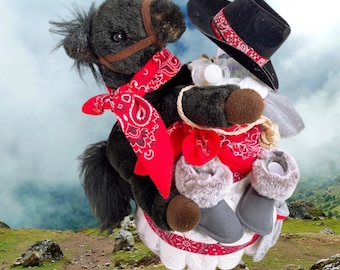May include: A black and white stuffed horse wearing a red bandana and a cowboy hat. The horse is holding a white diaper cake with grey booties and a red bandana.