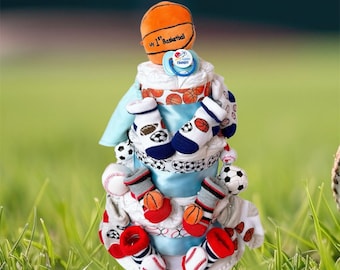 May include: A blue and white baby shower diaper cake decorated with a basketball, socks, and a pacifier. The cake is decorated with the words "my 1st basketball".